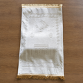 Thick white prayer rug with gold fringe and geometric border.