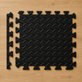 Black interlocking gym mat pieces arranged on a wooden floor.