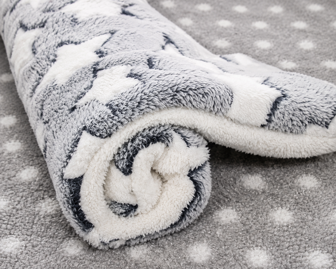 Rolled-up plush dog mat with a gray and white star pattern on a dotted background.