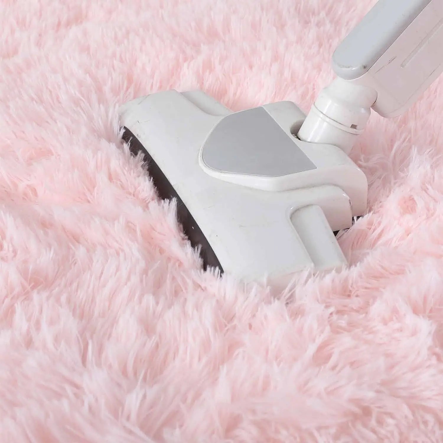 Close-up of a vacuum cleaner head cleaning a fluffy pink round living room rug.