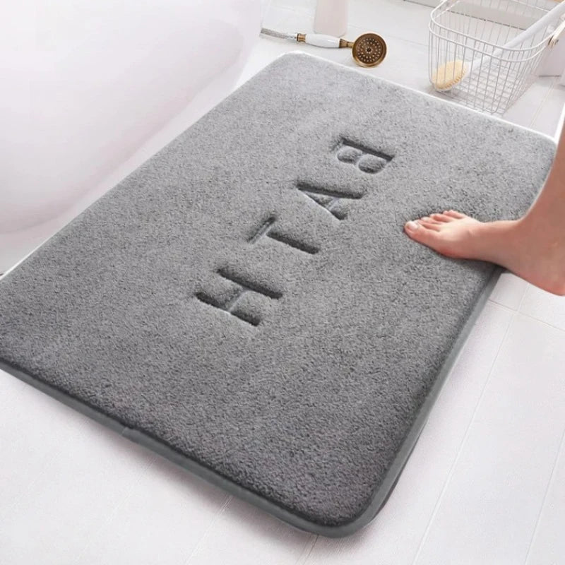 Plush gray bathroom mat with "BATH" embossed on it, next to a bathtub.