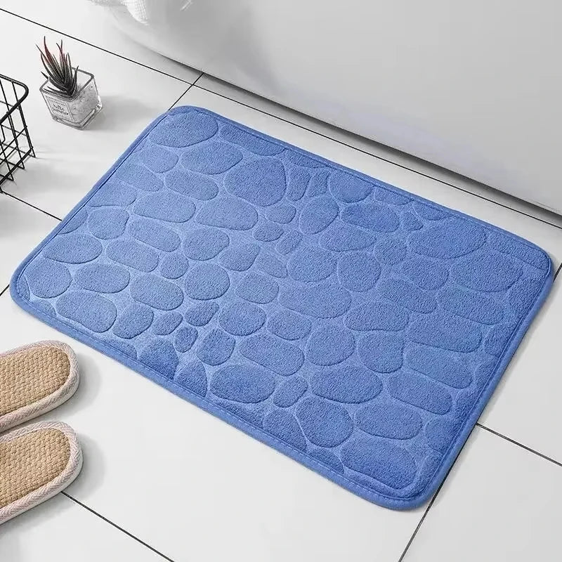 Blue pebble-textured bath mat placed on a white tiled floor next to a bathtub.