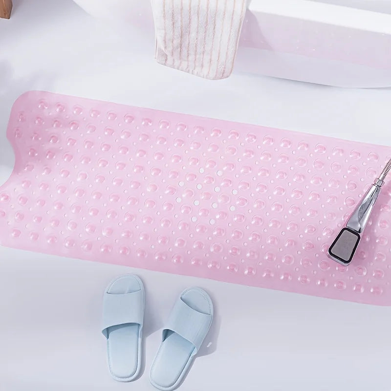 Pink non-slip bath mat with textured surface and suction cups, placed next to a shower head and slippers.