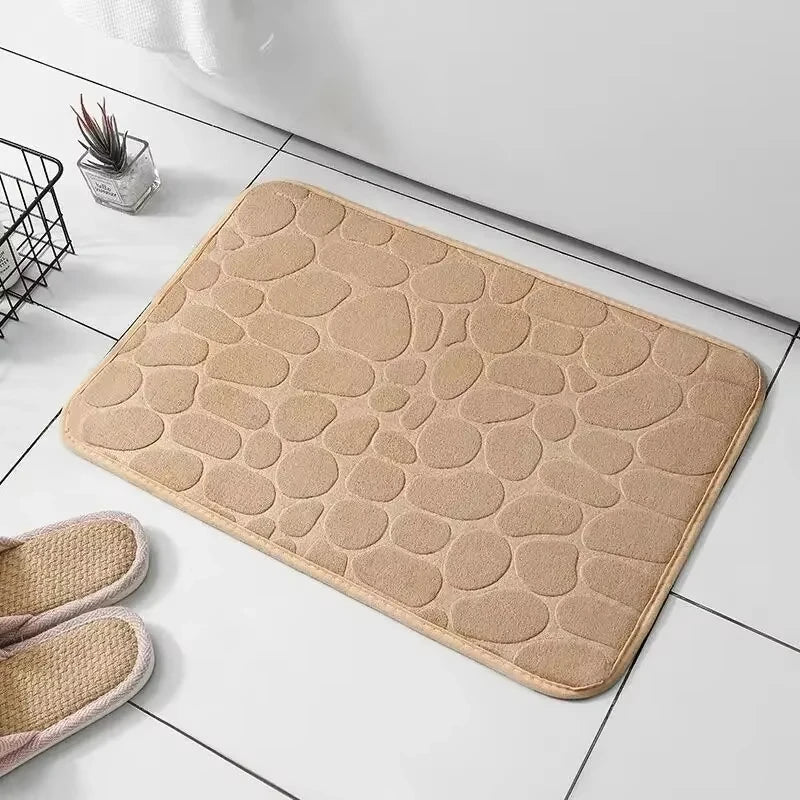 Beige stone-patterned bath mat for a bathroom, placed on white tiled floor.