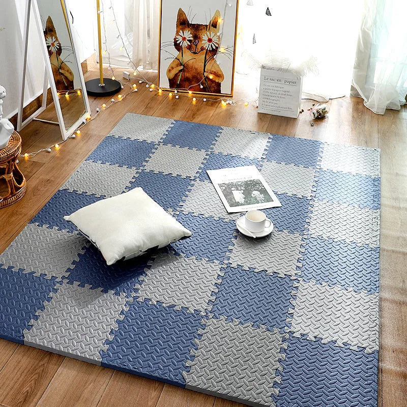 Blue and gray interlocking foam puzzle mat tiles arranged as a floor rug, with a white pillow and a magazine on top.