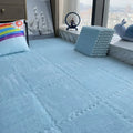 Soft blue interlocking floor mats, creating a plush play area with a rainbow pillow.